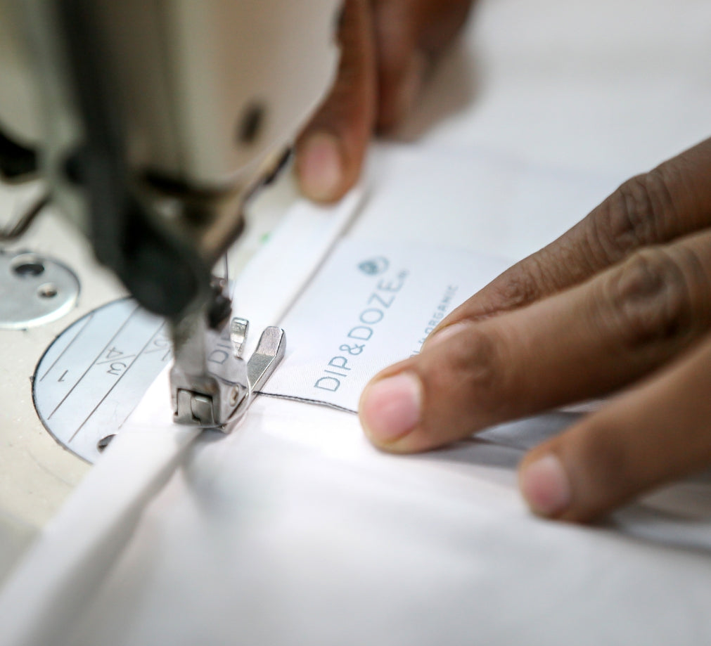 Close Up Of Women's Hands Sewing A Branded Label Onto Fabric On A Sewing Machine | Dip &amp; Doze